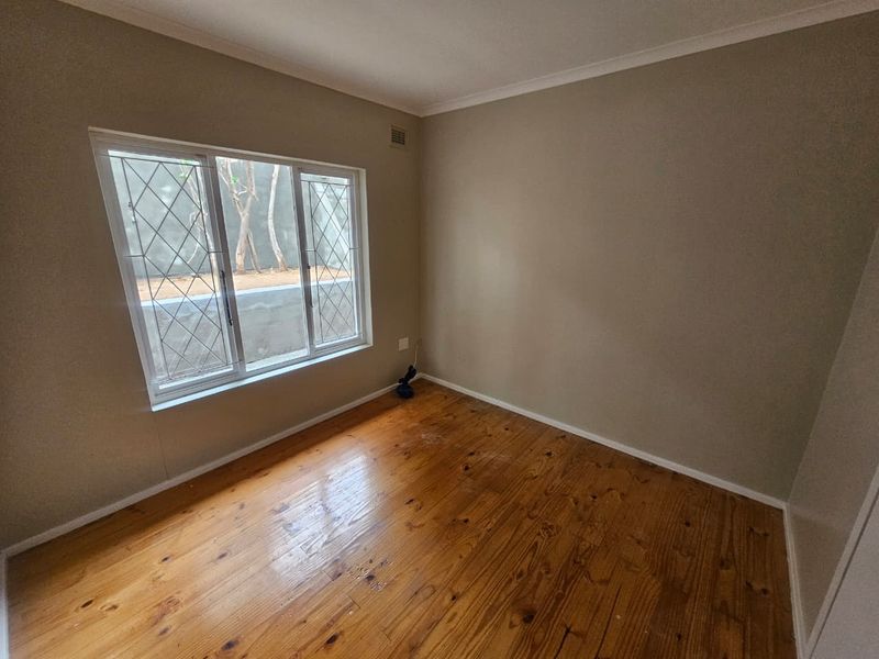 An empty bedroom featuring polished timber flooring, neutral walls, and windows fitted with security bars.