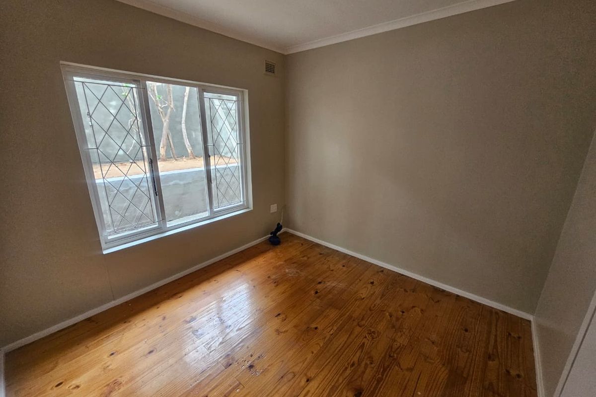An empty bedroom featuring polished timber flooring, neutral walls, and windows fitted with security bars.