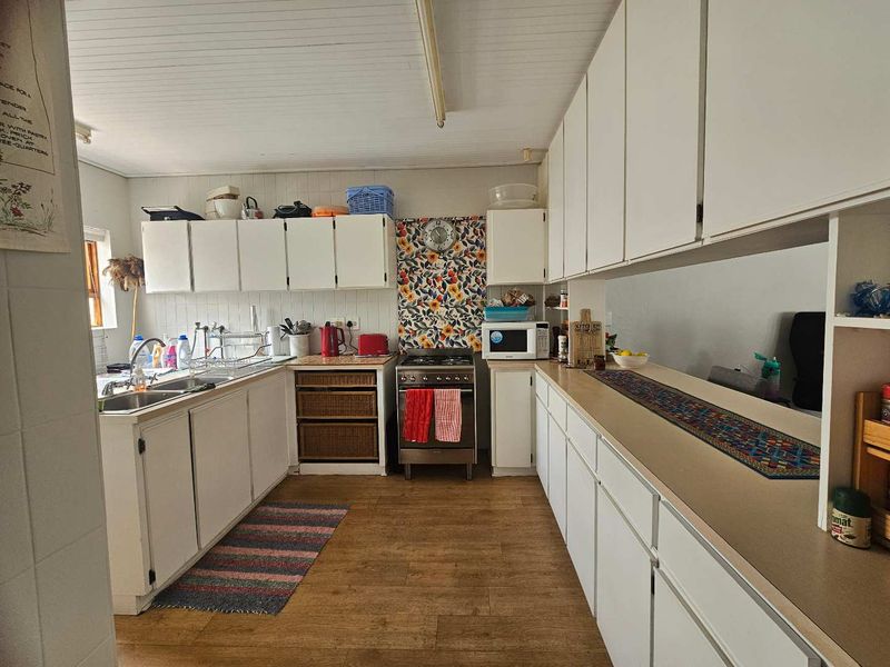 A functional kitchen featuring white cabinetry, a double sink, a freestanding stove, and a breakfast counter, offering a practical layout with potential for modernization.