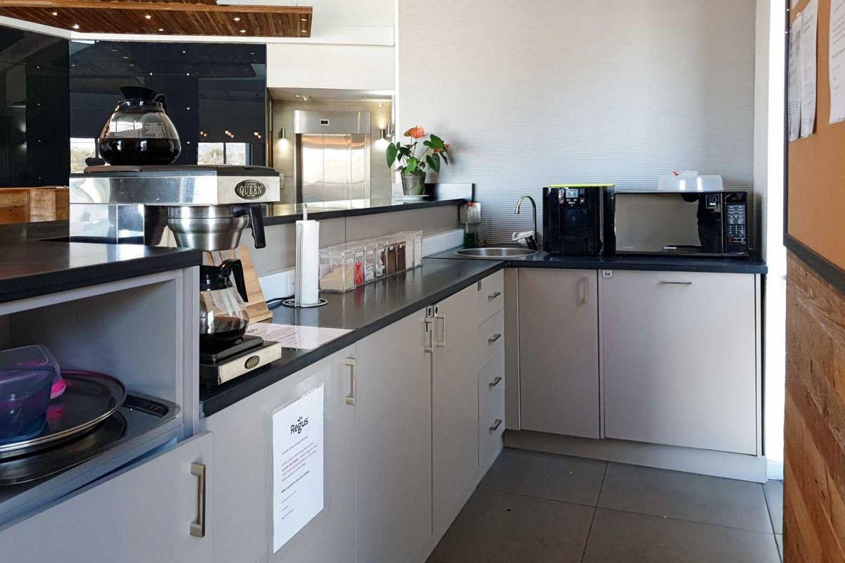 A functional office kitchenette featuring modern grey cabinetry, a dark countertop, a built-in sink, and tiled flooring.