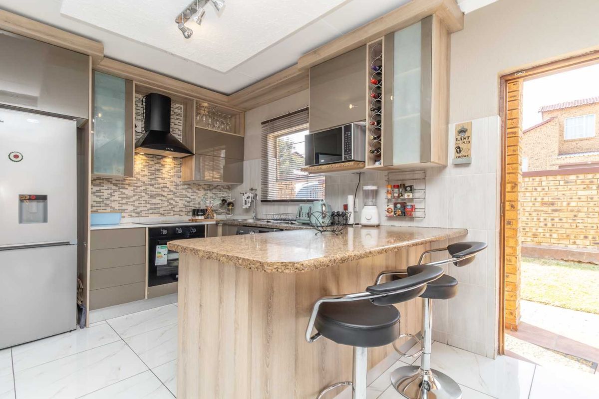 Modern kitchen featuring granite countertops, built-in cabinetry, a breakfast bar, and a tiled backsplash, with direct access to the rear garden.