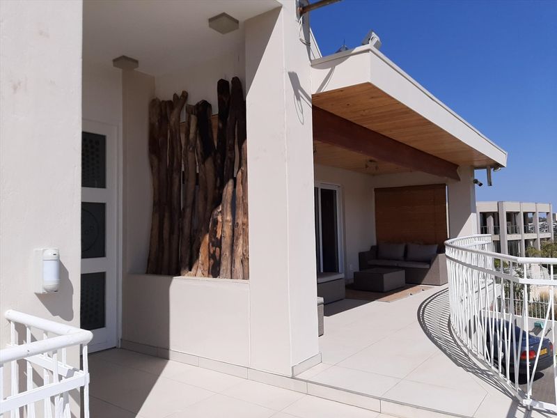 A spacious covered balcony featuring tiled flooring, timber ceiling accents, and a curved metal balustrade, offering a clean and well-maintained outdoor living space.