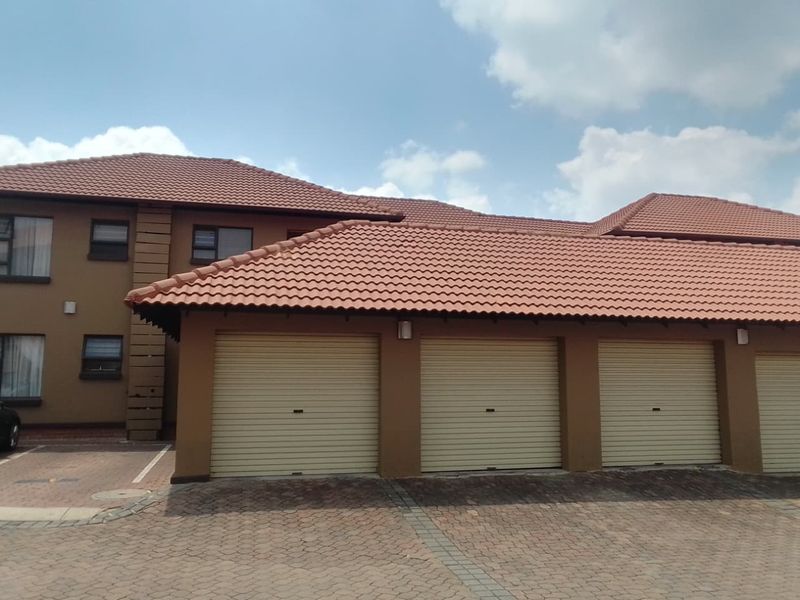 Exterior view of an apartment complex featuring a row of garages with roller doors and a paved driveway under a tiled roof.
