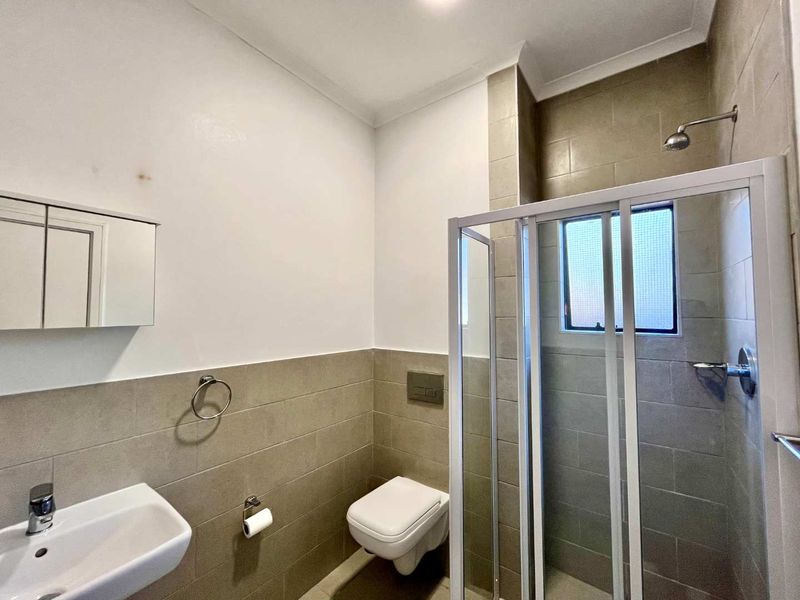 A functional bathroom featuring a wall-mounted toilet, a shower enclosure with a glass door, and a wall-mounted basin with a medicine cabinet.