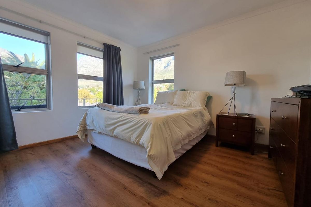 A bright bedroom featuring laminate flooring, large windows with mountain views, and neutral wall finishes.