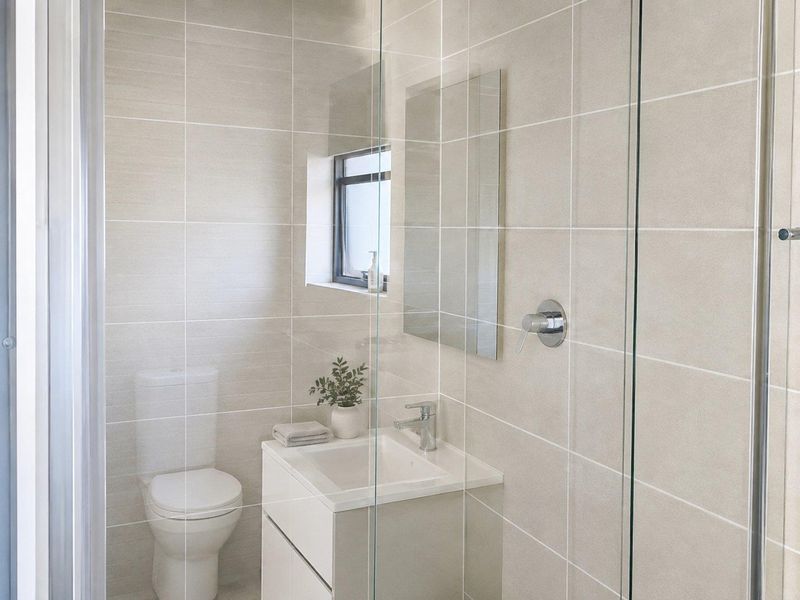 A modern, well-maintained bathroom featuring neutral wall tiles, a sleek wall-mounted vanity, and a glass-enclosed shower area.