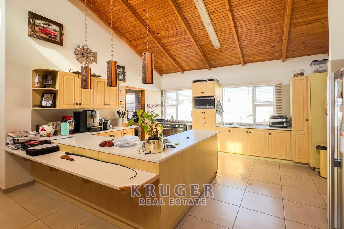 Spacious kitchen featuring light wood cabinetry, a large breakfast bar, tiled flooring, and a high vaulted timber-paneled ceiling.
