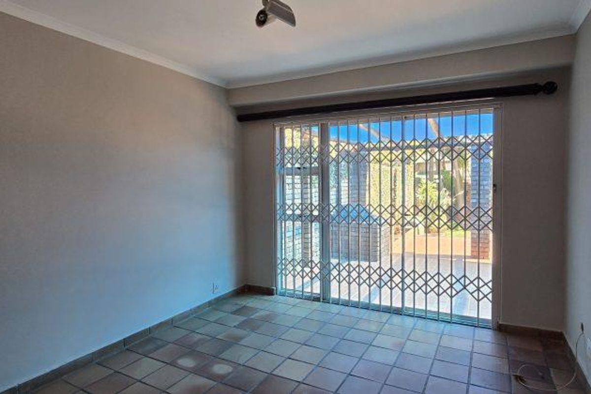 A vacant living room featuring tiled flooring and a sliding glass door with a security gate leading to an outdoor patio area.