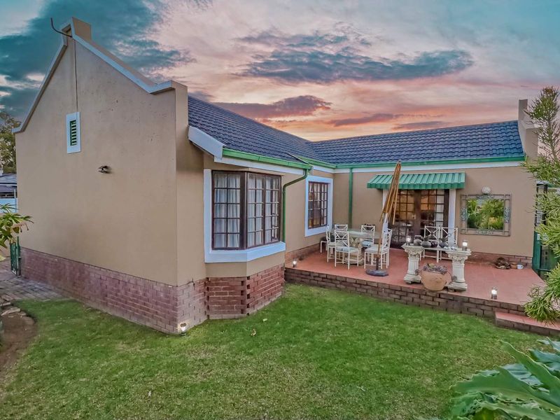 Rear view of the cluster home featuring a paved patio area, well-maintained garden, and classic architectural details including a bay window and tiled roof.