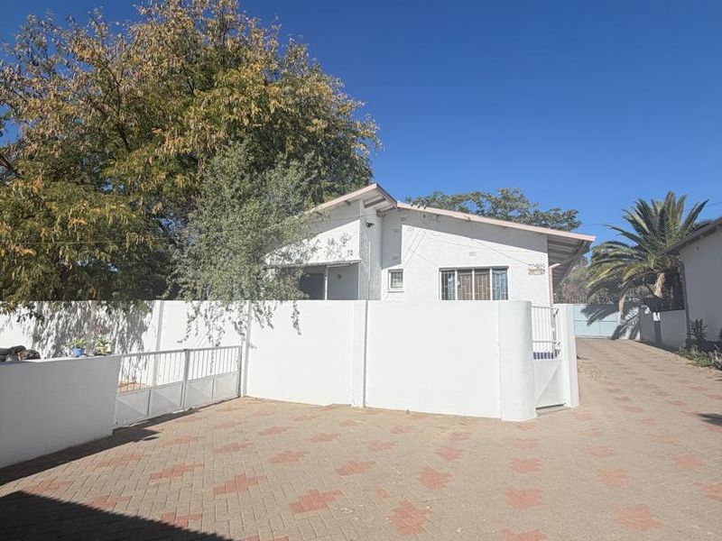 Front view of the property featuring a paved driveway, secure perimeter wall, and gated entrance.