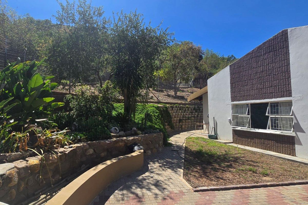 Rear exterior view featuring a paved walkway, stone retaining walls, landscaped garden area, and a building facade with stone-textured cladding and casement windows.