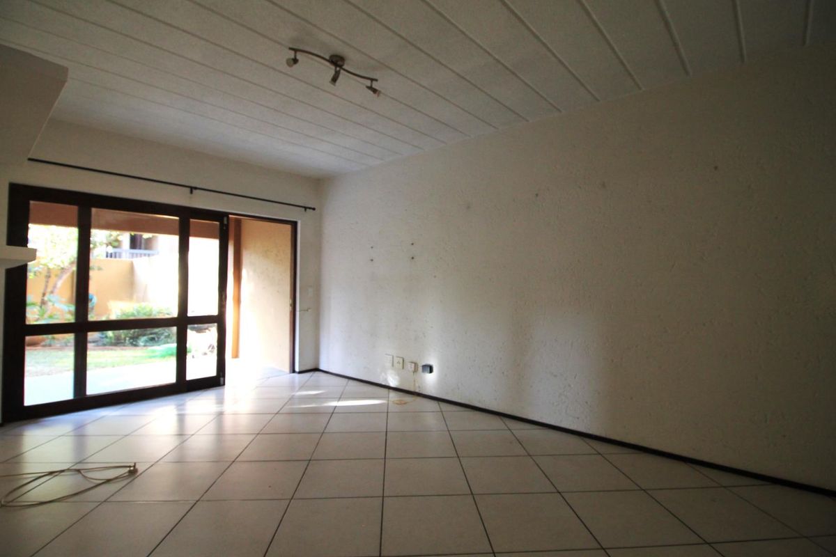 An empty living room featuring tiled flooring, textured walls, and a sliding glass door providing access to an outdoor area.