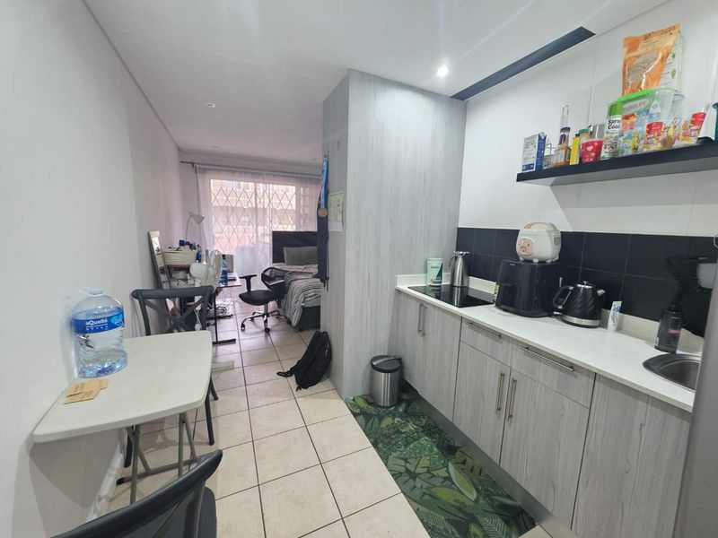 Compact open-plan apartment featuring a functional kitchenette with modern cabinetry, tiled flooring, and a seamless transition into the bedroom area.