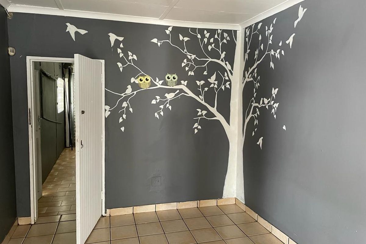 A bedroom featuring tiled flooring and a decorative painted wall mural, with an open doorway leading to an adjacent hallway.