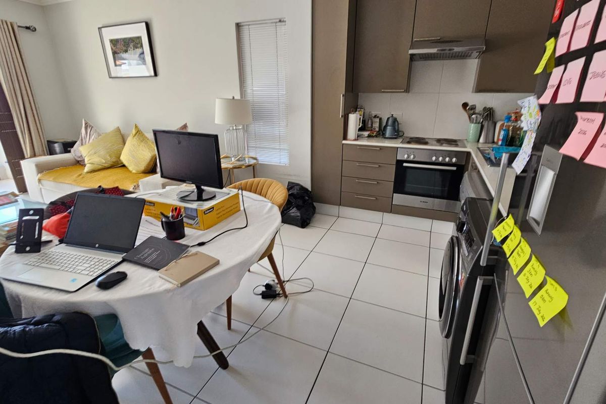 Open-plan living area featuring a compact kitchen with built-in oven, hob, and extractor fan, leading to a balcony through a sliding door.