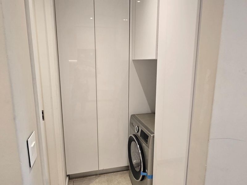 A compact, modern laundry nook featuring sleek white built-in cabinetry and space for a washing machine.