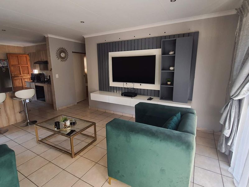 Open-plan living area featuring a modern built-in media wall, tiled flooring, and a seamless transition to the adjacent kitchen space.