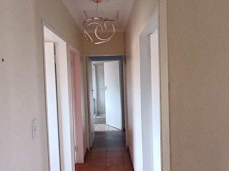 A narrow residential hallway with tiled flooring and neutral walls, providing access to multiple rooms within the townhouse.