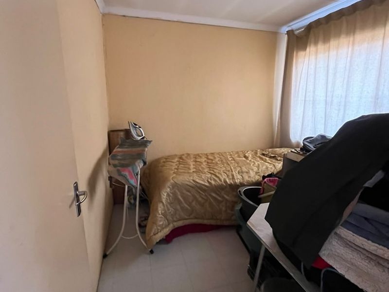 A compact bedroom featuring tiled flooring and a window with a curtain rail, offering a functional space for a single bed.