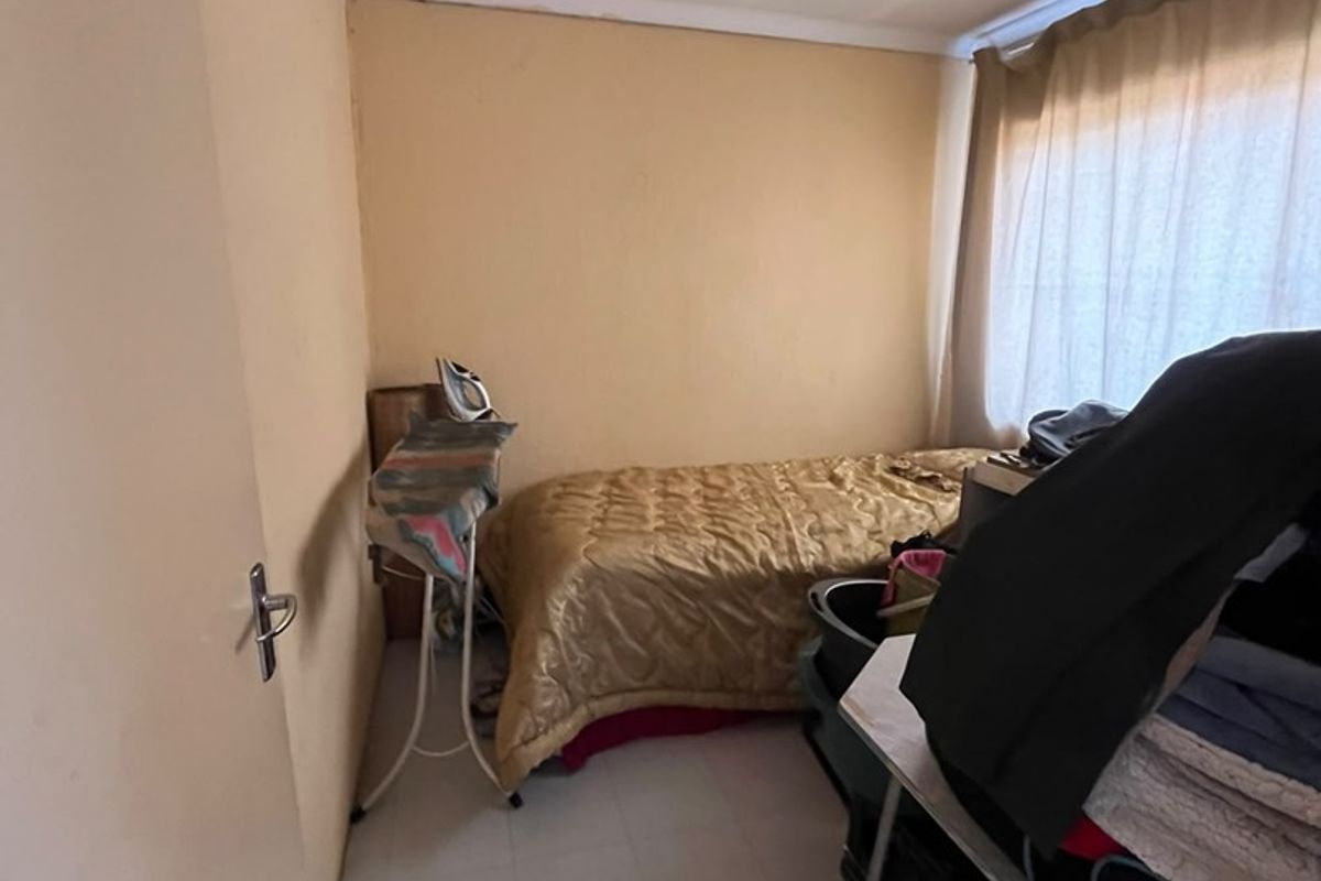 A compact bedroom featuring tiled flooring and a window with a curtain rail, offering a functional space for a single bed.