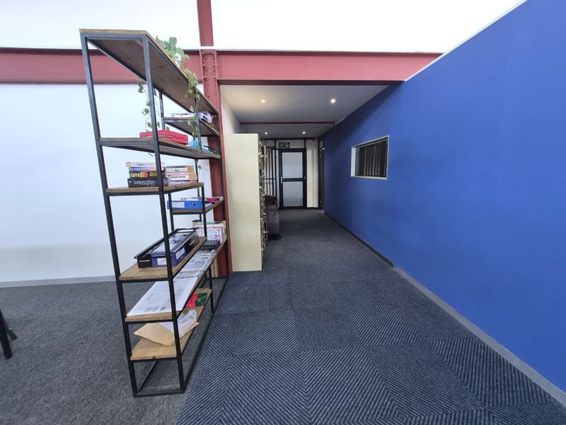 A modern office hallway featuring exposed structural steel beams, recessed lighting, and blue accent walling with carpeted flooring.