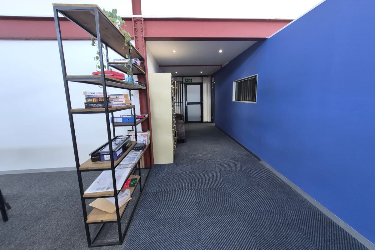 A modern office hallway featuring exposed structural steel beams, recessed lighting, and blue accent walling with carpeted flooring.