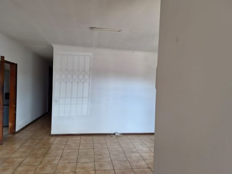 An empty living area featuring ceramic floor tiles, neutral walls, and a security gate, offering a blank canvas for potential interior design updates.