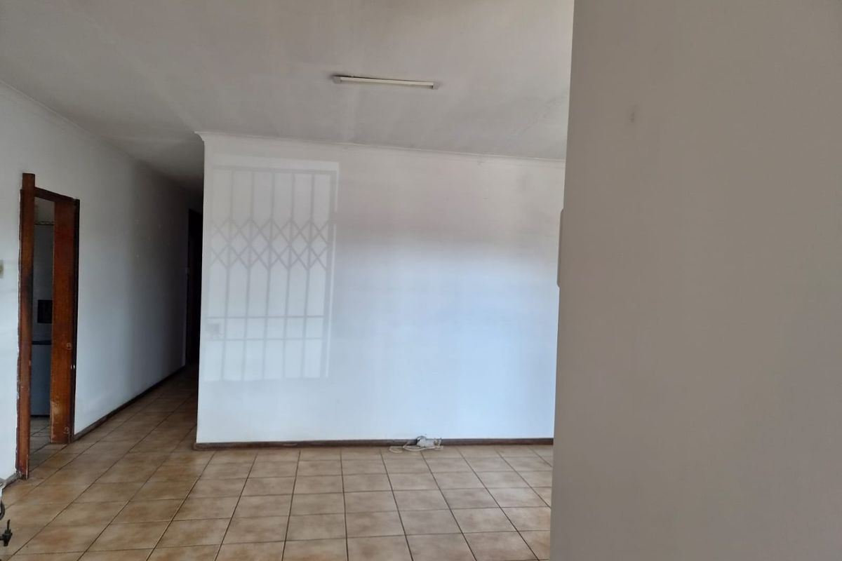 An empty living area featuring ceramic floor tiles, neutral walls, and a security gate, offering a blank canvas for potential interior design updates.