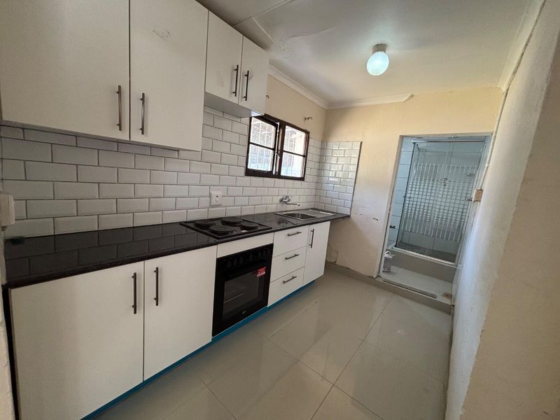 Compact kitchen featuring white cabinetry, subway tile backsplash, granite countertops, and integrated appliances, with an adjacent shower area.