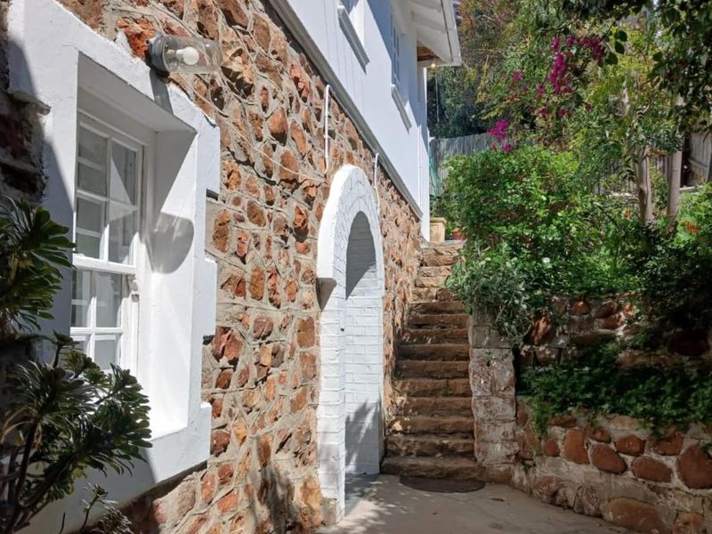 A charming exterior view featuring rustic stone masonry walls, an arched doorway, and stone steps leading up through a landscaped garden area.