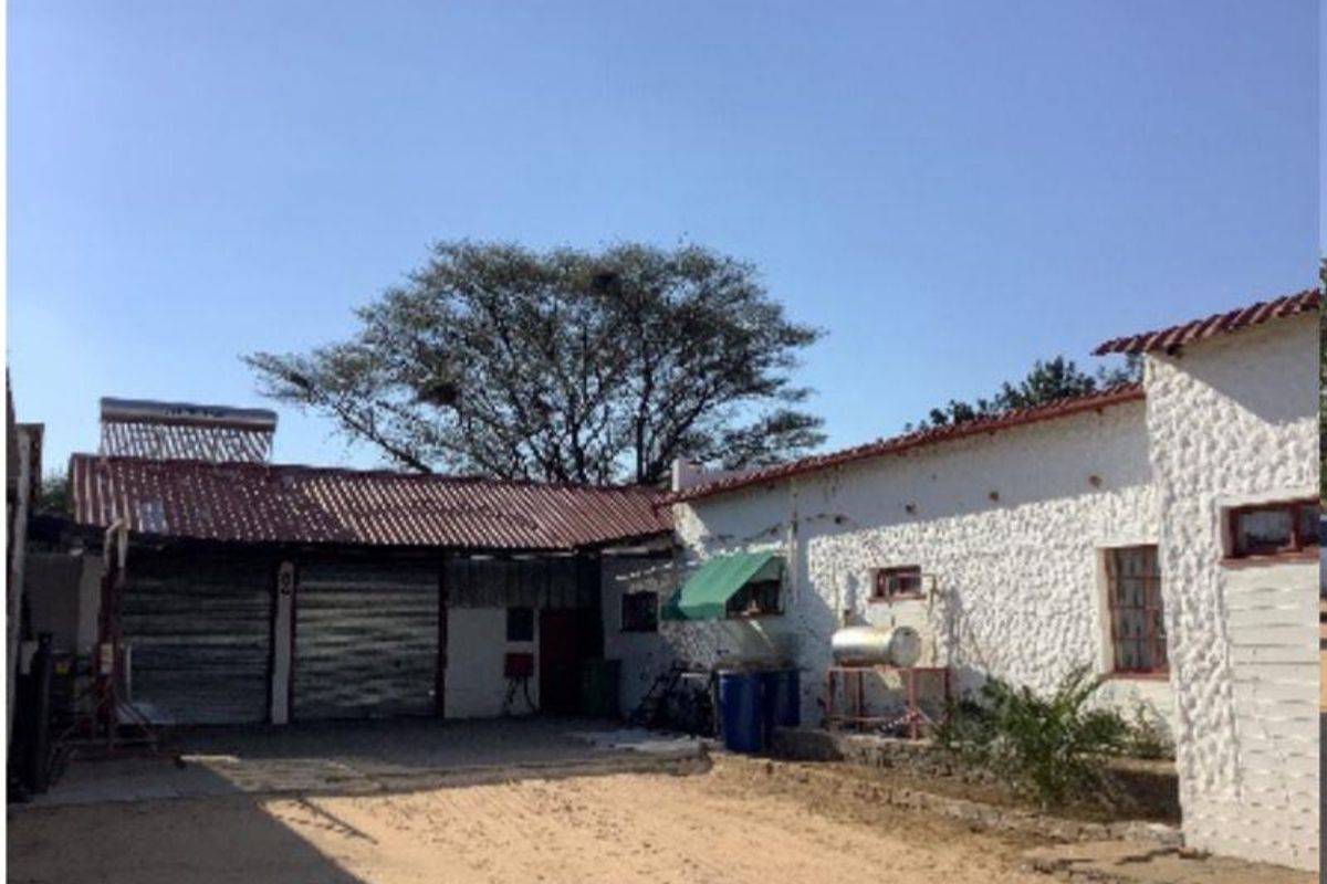 Rear view of the farm property featuring textured white masonry walls, corrugated metal roofing, and integrated solar water heating infrastructure.