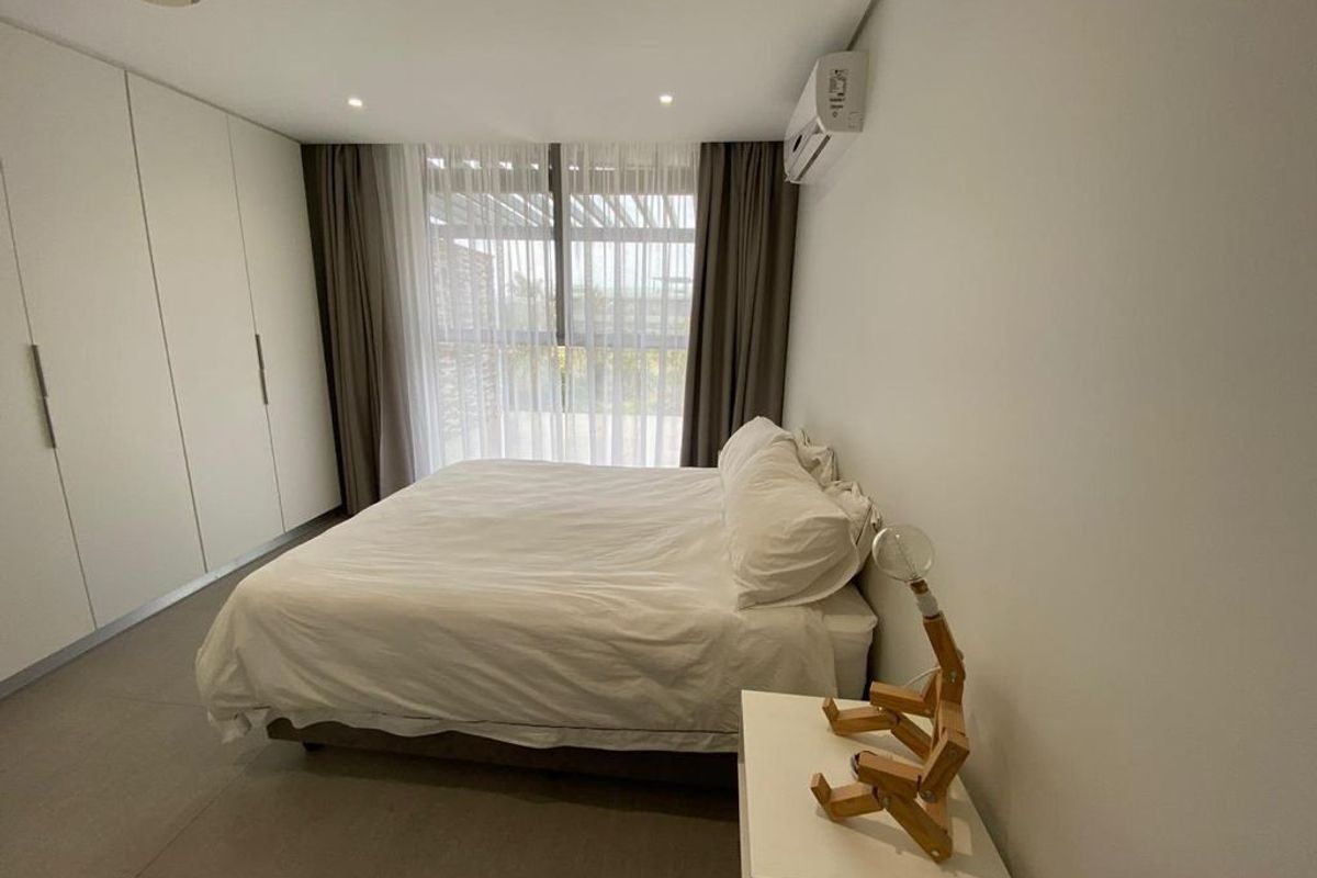 A modern bedroom featuring built-in wardrobes, tiled flooring, recessed lighting, and a wall-mounted split-system air conditioner with access to a balcony.