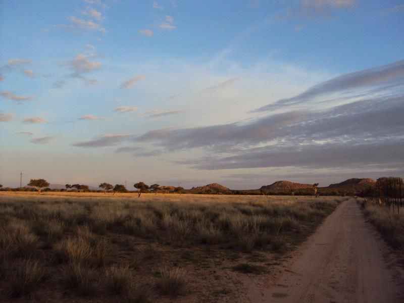 A scenic view of the expansive small holding landscape featuring a dirt access road, natural grasslands, and distant mountain vistas under a clear sky.