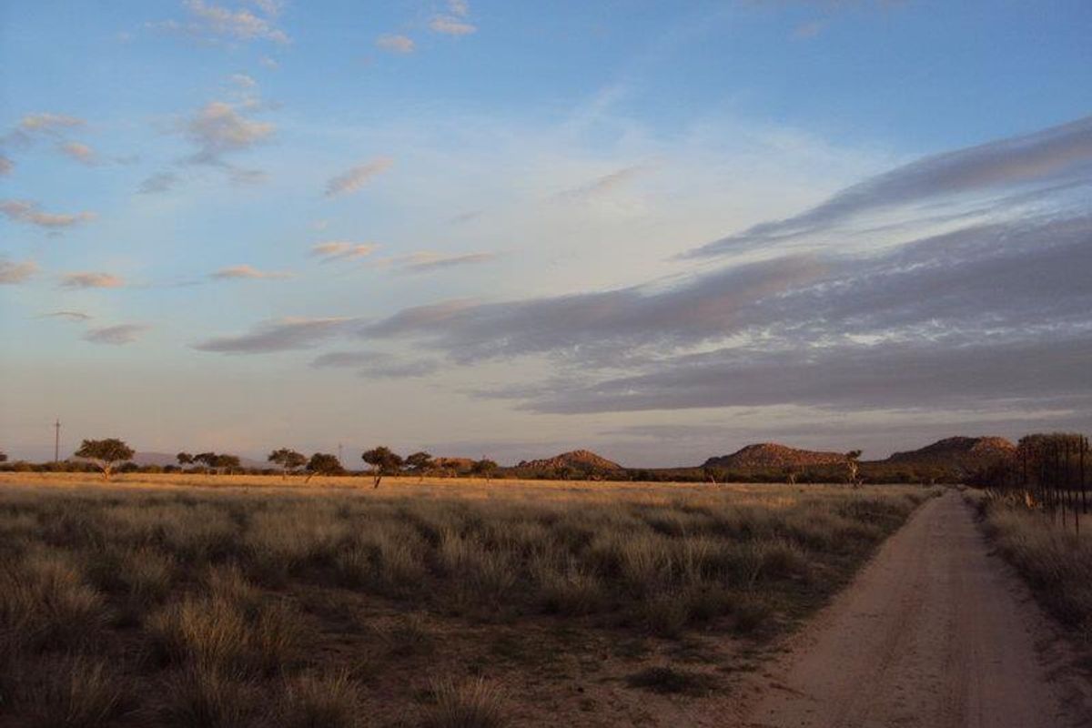 A scenic view of the expansive small holding landscape featuring a dirt access road, natural grasslands, and distant mountain vistas under a clear sky.