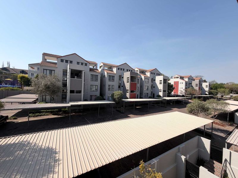 Exterior view of a multi-story apartment complex featuring covered parking bays and paved driveway areas.