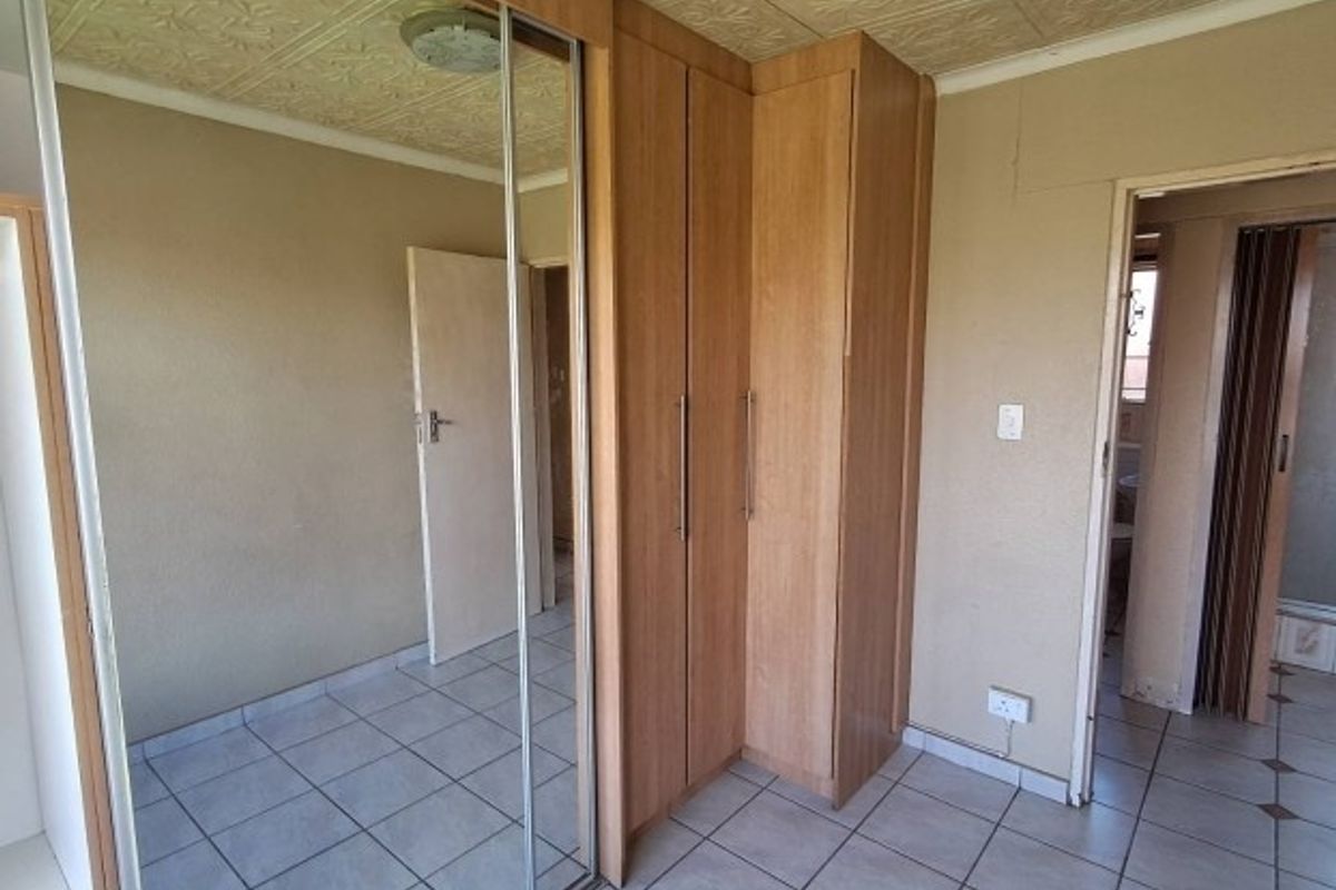 A bedroom featuring built-in cupboards with mirrored doors, tiled flooring, and textured ceiling tiles, presenting a dated interior ready for modernization.