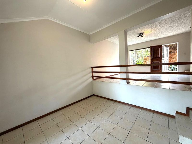 An empty, split-level living area featuring tiled flooring, a timber balustrade, and direct access to an outdoor space through a wooden door.
