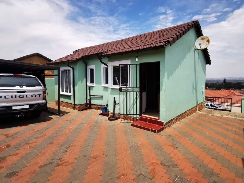 Front exterior view of the house featuring a paved driveway, carport, and tiled roof structure.