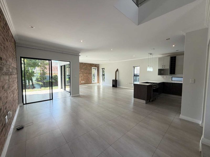 Spacious open-plan living and kitchen area featuring large sliding doors to the garden, exposed brick accents, a modern kitchen island, and a freestanding fireplace.