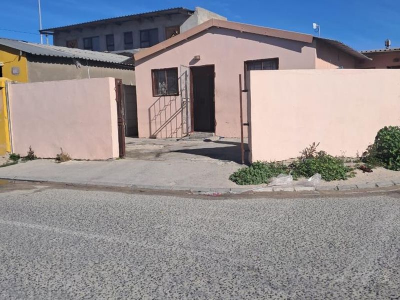 Front view of a single-story house featuring a perimeter wall, gated entrance, and concrete driveway area.