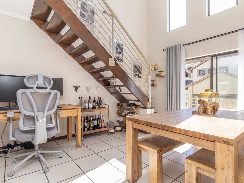 Open plan living area featuring a wooden staircase, tiled flooring, and large windows providing natural light with access to an outdoor balcony.