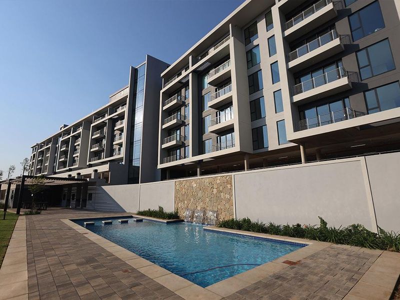 Modern apartment complex featuring a well-maintained swimming pool with a stone water feature and paved deck area.