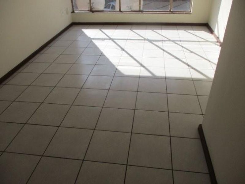 An empty, sunlit living area featuring neutral ceramic floor tiles and a large window, providing a blank canvas for interior design.