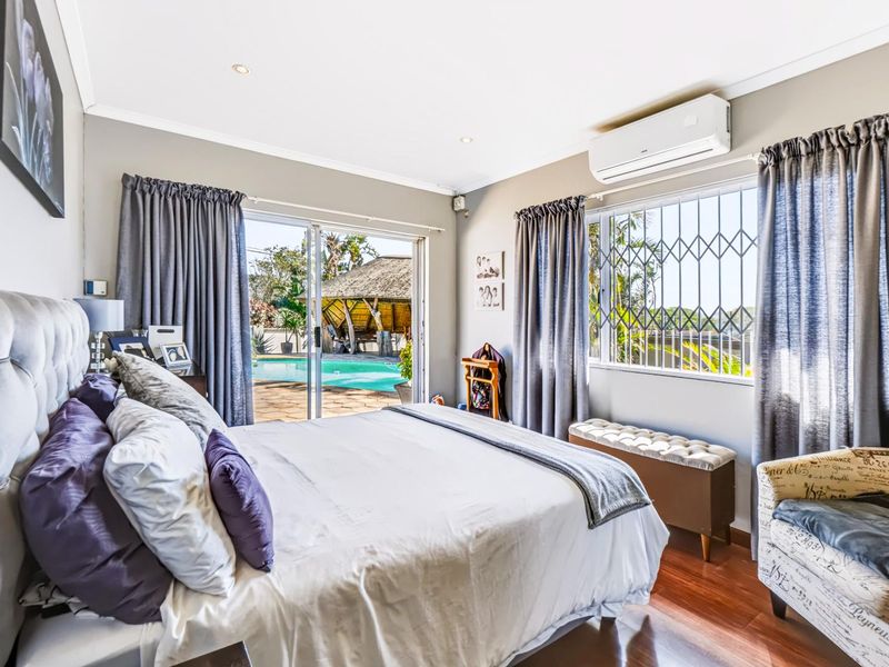 Bright bedroom featuring hardwood flooring, a split-system air conditioner, and sliding glass doors providing direct access to the outdoor pool area.