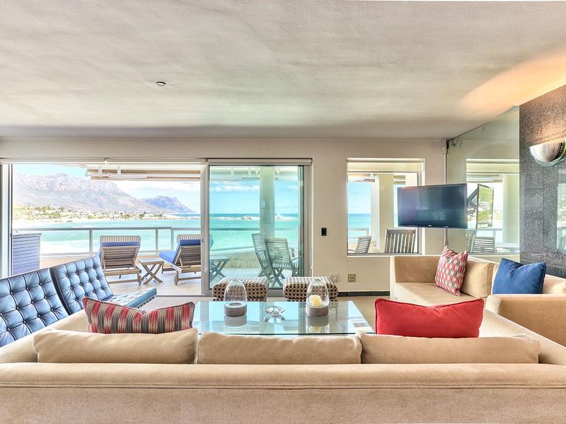 Spacious living room featuring a stone accent wall and large sliding glass doors that open to a balcony with panoramic ocean and mountain views.