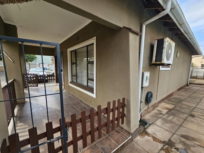 A side view of the property featuring a covered tiled patio, security gate, and an external air conditioning unit mounted on the exterior wall.