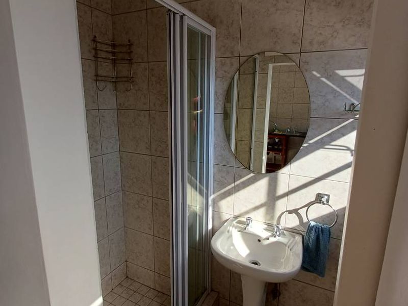 A functional bathroom featuring a pedestal basin, a shower enclosure with glass doors, and neutral wall and floor tiling.