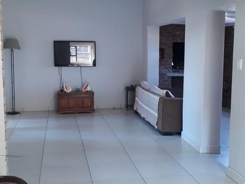Spacious open-plan living area featuring large ceramic floor tiles and an exposed brick feature wall, providing a versatile layout for modern living.