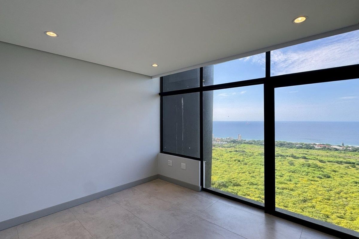 A bright, empty bedroom featuring floor-to-ceiling windows with expansive coastal and landscape views, modern tiled flooring, and recessed lighting.