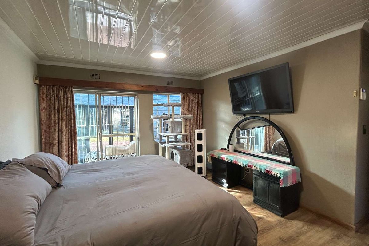 Spacious bedroom featuring laminate flooring, glossy ceiling panels, and a sliding glass door providing direct access to the outdoor area.